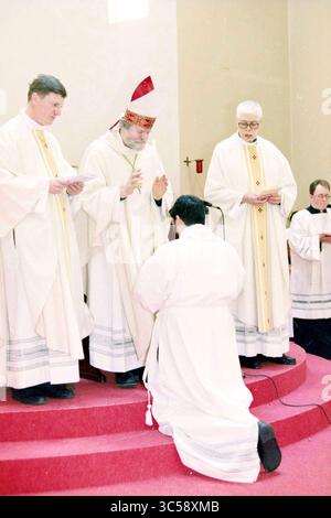 Ordination von vier Diakonen, Heiloo, Heiloo, 24-03-1999 Whizgle News, niederländisches Büro, Niederlande, 1950-2000 Eine Gruppe von Geistlichen versammelt sich in einem zeremoniellen Rahmen, wobei ein Priester vor einem anderen kniet, der in kunstvollen Gewändern gekleidet ist und offenbar einen Segen vollbringt. Die Atmosphäre ist feierlich und ehrfurchtsvoll und betont ein bedeutendes religiöses Ritual. Andere Geistliche stehen zur Verfügung und beobachten die Zeremonie. Stockfoto