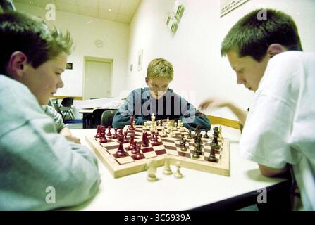 Schachclub, IJmuiden, IJmuiden, Niederlande, 23-01-2001 Whizgle News, Dutch Desk, Niederlande, 1950-2000 drei Jungen konzentrieren sich intensiv auf ein Schachspiel und planen ihre Bewegungen, während sie um ein hölzernes Schachbrett sitzen. Das Brett ist mit einer Mischung aus dunklen und hellen Stücken besetzt, und jeder Spieler scheint tief in Gedanken zu sein und denkt über seine nächste Aktion nach. Die Atmosphäre ist eine von Konzentration und freundlichem Wettbewerb. Stockfoto