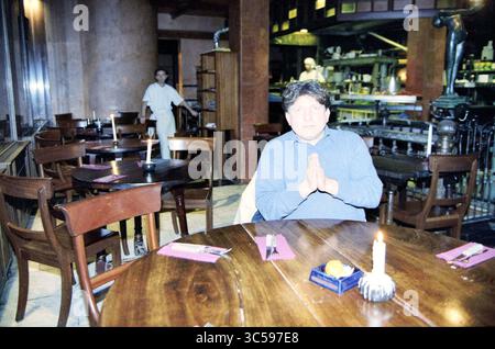 Restaurant Picollo schließt, Haarlem, Riviervismarkt, Niederlande, 13-12-1999 Whizgle News, Dutch Desk, Niederlande, 1950-2000 Ein Mann sitzt an einem Holztisch mit den Händen, die in einer Geste der Kontemplation oder des Gebets zusammengelegt sind, umgeben von einer gemütlichen Atmosphäre. Im Hintergrund erfüllt ein Mitarbeiter seine Aufgaben und trägt zur warmen Atmosphäre des Restaurants bei. Eine beleuchtete Kerze und ein kleines Gericht werden an den Tisch gestellt, was das Gefühl eines intimen Essens unterstreicht. Stockfoto