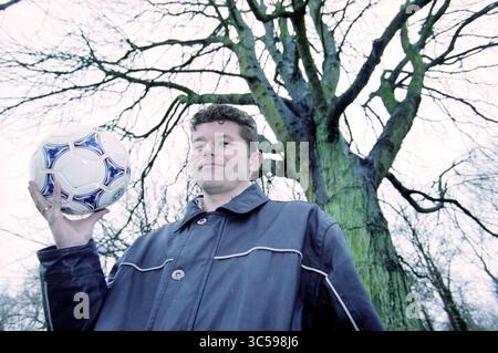 Ed Kist Football and Profession, Bennebroek, Bennebroek, 05-12-1999 Whizgle News, Dutch Desk, Niederlande, 1950-2000 Ein Mann steht zuversichtlich, hält einen Fußball, vor einem großen, blattlosen Baum, der über ihm thront. Sein Ausdruck deutet auf Entschlossenheit hin, da die krasse Landschaft eine reflektierende Stimmung erzeugt. Stockfoto