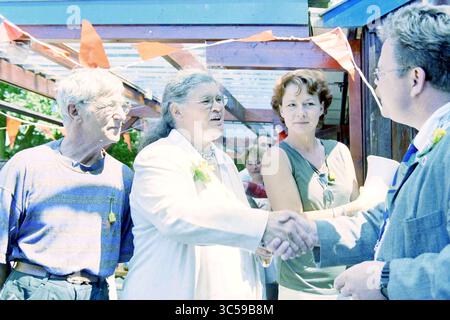 Tante Eef, Medaille, Santpoort-Noord, Santpoort-Noord, 23-07-1999 Whizgle News, Dutch Desk, Niederlande, 1950-2000 Eine Gruppe von Menschen versammelt sich im Freien, um ein freundliches Gespräch zu führen. Eine Frau in einem weißen Outfit schüttelt einer anderen Person warm die Hände, während andere zuschauen, was ein Gefühl von Kameradschaft schafft. Farbenfrohe Dekorationen und ein zwangloses Ambiente lassen eine festliche Atmosphäre vermuten. Stockfoto