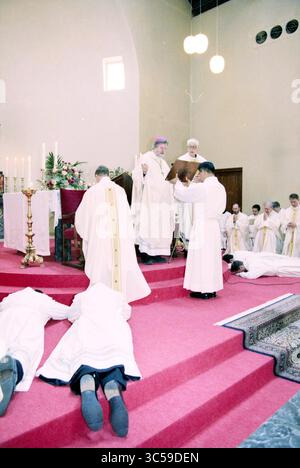 Ordination von vier Diakonen, Heiloo, Heiloo, 24-03-1999 Whizgle News, niederländisches Büro, Niederlande, 1950-2000 Eine feierliche Versammlung in einer Kirche, bei der Geistliche in weißen Gewändern an einem Gottesdienst teilnehmen. Mehrere Menschen knien in Demut, während andere, darunter ein Bischof, die Arbeiten am Altar leiten, umgeben von Kerzen und Blumenarrangements. Stockfoto
