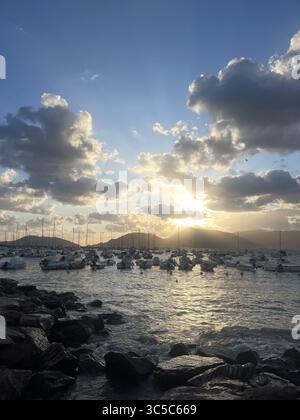 Die Boote liegen in einer ruhigen Bucht vor einem atemberaubenden Sonnenuntergang. Der Himmel ist voller dramatischer Wolken, und sanfte Wellen treffen auf das felsige Sho Stockfoto