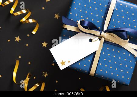 Banner mit blauer Geschenkbox mit goldenem Band, leerem Geschenkanhänger und goldenen Konfetti-Sternen. Platzieren für Ihren Text Stockfoto