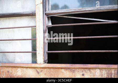 Dies ist eine Beschreibung eines rostigen Fensters mit einem robusten Holzrahmen, ergänzt durch starke Metallstangen für zusätzliche Sicherheit Stockfoto