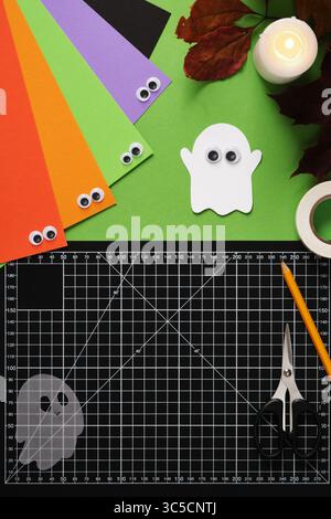 Handgemachte Papiergeister mit guten Augen auf grünem Hintergrund. Schreibtisch für Papierarbeiten. Draufsicht, Platz für Text. Stockfoto
