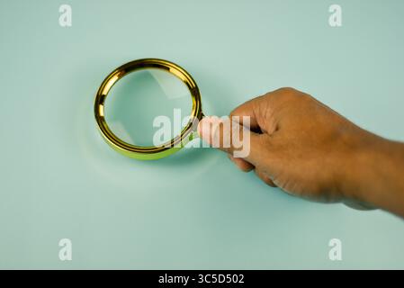 Nahaufnahme einer Lupe, die ihren goldenen Rahmen vor einem hellblaugrünen Hintergrund hervorhebt. Stockfoto