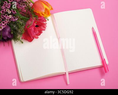 Bunte Tulpen liegen auf leerer Notizbuchseite, rosa Hintergrund. Platz für Ihren Text. Stockfoto