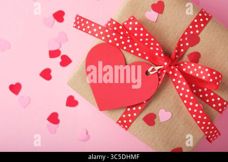 Banner mit brauner Geschenkbox mit herzförmigem Anhänger auf rosa Hintergrund. Platzieren für Ihren Text Stockfoto