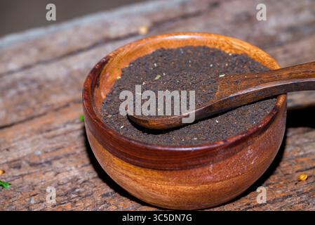 indischer schwarzer Tee, Teelöffel mit Teeblättern auf Holztisch. Schwarzes Teepulver auf hölzernem Hintergrund. Nahaufnahme Stockfoto
