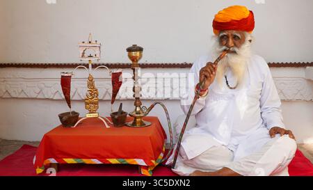 Ein weiser, alter Indianer in traditioneller Kleidung, der mit Pfeife sitzt, nachdenklich, nachdenklich aussieht, in Jodhpur, Rajasthan, Indien Stockfoto