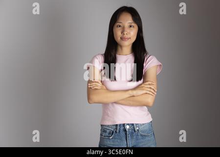 Eine junge asiatische Frau mit langen, dunklen Haaren steht mit überkreuzten Armen nach vorne Stockfoto