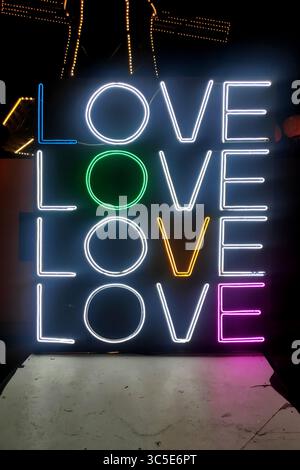 Nahaufnahme eines weißen Neonlichts, das viermal in die Worte „Liebe“ geformt ist, mit einem Farbbuchstaben, der von oben links nach unten rechts für „Liebe“ verläuft Stockfoto