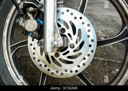 Nahaufnahme des Vorderrads des Motorrads mit Bremsscheibe und Bremssattel auf Betonhintergrund. Stockfoto