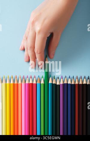 Grünes Bleistiftmuster von Hand aus einer Reihe mehrfarbiger Bleistifte auf hellblauem Hintergrund. Stockfoto