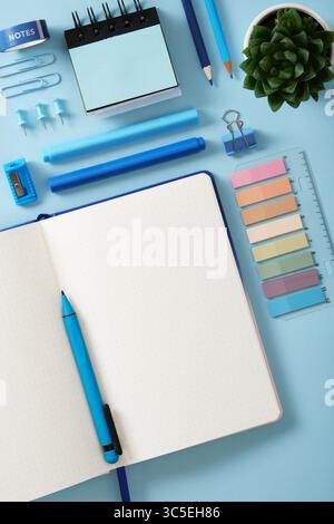 Blick von oben auf einen hübschen Schreibtisch. Offenes Notizbuch mit einer leeren Seite, blauen Schreibstiften, Bleistiften, Filzstiften, Spitzer, Aufklebern. Stockfoto