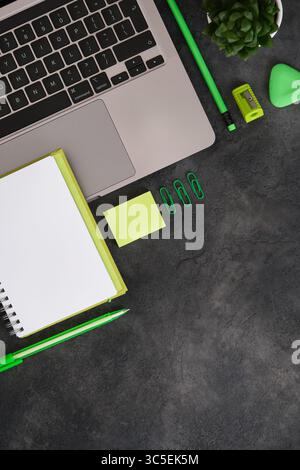 Arbeitsbereich mit Laptop, grünem Schreibmaterial, Notizblock und saftigem Stoff auf dunklem Hintergrund. Kopierbereich. Stockfoto