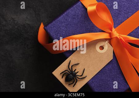 Halloween-Geschenk in lilafarbenes Papier mit orangefarbenem Band und leerem Etikett mit Spinne Stockfoto