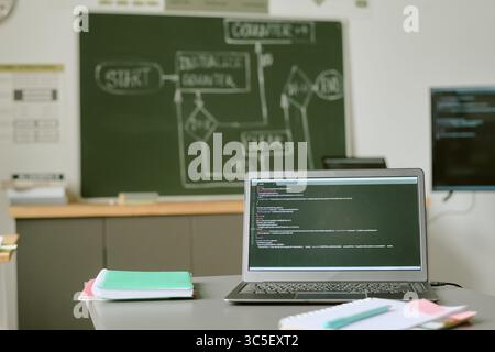Laptop zeigt Programmiercode im Klassenzimmer mit Blackboard im Hintergrund an Stockfoto