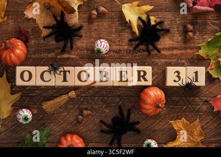 Text 31 Oktober mit Holzwürfeln geschrieben. Halloween Vibes, Kürbisse, Augen, große schwarze Spinnen, Hexenbesen, Herbstlaub Stockfoto