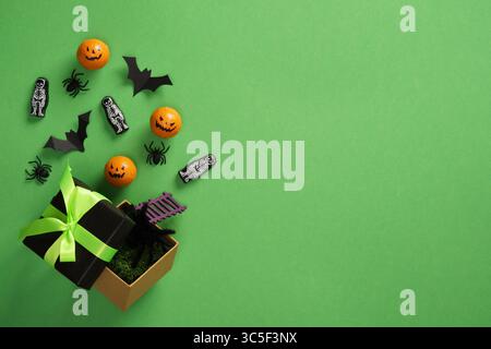 Halloween-Karte: Kürbisse, schwarze Fledermäuse, Spinnen, Skelette fliegen aus der Geschenkbox auf grünem Hintergrund. Platz für Ihre SMS, Einladung, Werbung. Stockfoto
