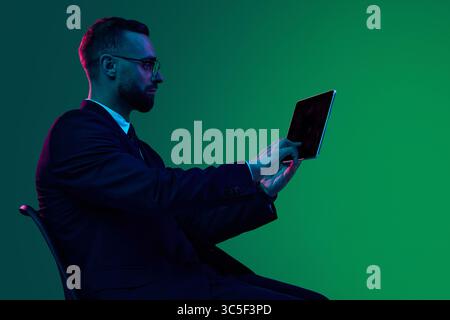 Geschäftsmann, der ein Tablet vor einem leuchtend grünen Hintergrund mit Farbverlauf verwendet Stockfoto