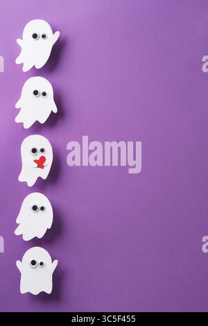 Niedliche Geister mit Augen auf violettem Hintergrund, ein Geist mit rotem Herz, vertikales Halloween-Banner, Platz für deinen Text Stockfoto