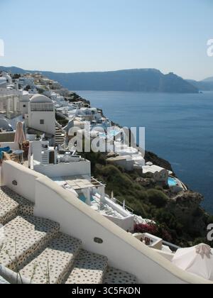 Weiße Treppe, die in Richtung der tiefblauen Ägäis in Santorin, Griechenland, führt. Traditionelle kykladische Architektur, klarer blauer Himmel und friedliche Meereslandschaft Stockfoto