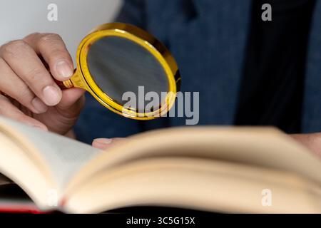 Ein älterer Mann, der mit einer Lupe ein Buch liest, das Sehschwierigkeiten und das Altern des Sehvermögens veranschaulicht. Stockfoto