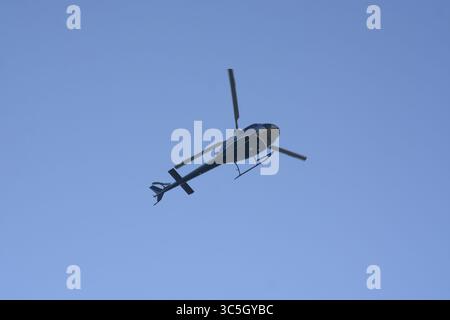 Hubschrauber fliegt über einem städtischen Gebiet mit blauem Himmel im Hintergrund Stockfoto