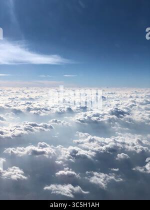 Eine ruhige Luftaufnahme von verstreuten Wolken, die in einem klaren blauen Himmel schweben, während des Fluges aus einem Flugzeugfenster aufgenommen. Stockfoto