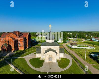 Eine Frontalansicht aus der Luft zeigt eine alte Kirche in Jurjew Polsky, die vor einem Hintergrund grüner Felder und weit entfernter Strukturen sichtbar ist Stockfoto
