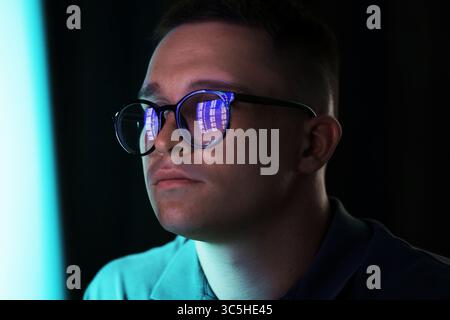 Junger Mann, der eine Brille trägt, mit Reflexion auf dunklem Hintergrund, Nahaufnahme Stockfoto