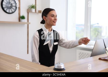 Lächelnder Rezeptionist in Uniform, der am Rezeptionstresen im Hotel den Kartenschlüssel gibt Stockfoto