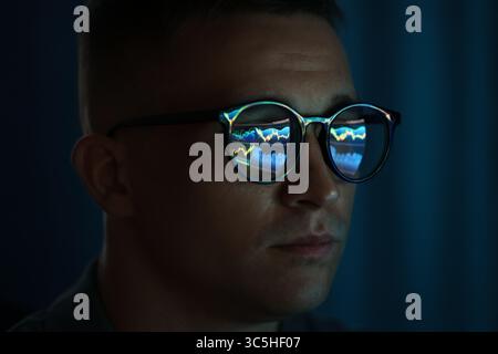 Junger Mann, der eine Brille trägt, mit Reflexion auf dunklem Hintergrund, Nahaufnahme Stockfoto