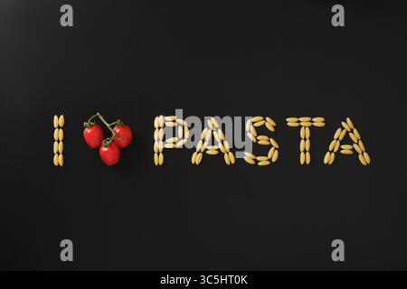 Satz Ich liebe Pasta aus trockenen Nudeln und Kirschtomaten, die wie ein Herz auf schwarzem Hintergrund geformt sind. Konzept der kulinarischen Leidenschaft und der italienischen Küche. Stockfoto