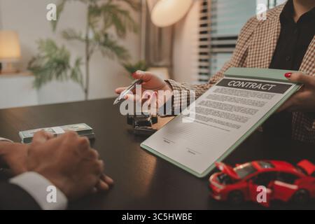 Ein Autoverkäufer erklärt dem Käufer die Details eines Autokaufvertrags, bevor er den Kaufvertrag, den Ausstellungsraum, den Händler, den Autokaufvertrag unterzeichnet, Stockfoto