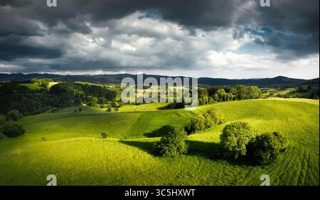 Blick aus der Vogelperspektive auf die grünen Hügel in wunderschönem dramatischem Licht, mit grünen Wiesen unter dunklen Wolken Stockfoto