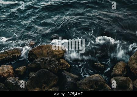 Dynamische Wellen krachen gegen zerklüftete Felsen und schaffen eine dramatische und kraftvolle Küstenlandschaft. Stockfoto