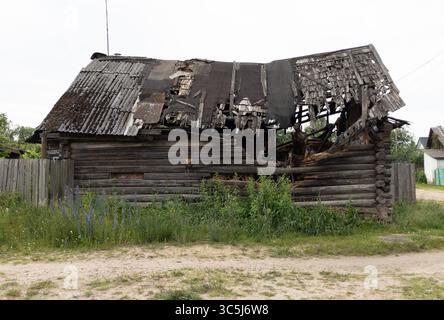 Verbranntes Holzhaus, zerstörtes Dorfhaus mit eingestürztem Dach, leeren Fenstern und eingestürztem Dach nach Feuer. Stockfoto