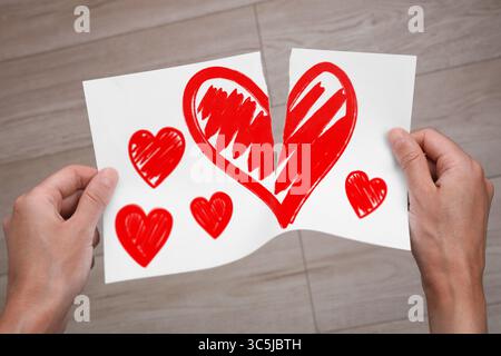 Verrat. Mann, der drinnen ein Blatt Papier mit roten Herzen zerreißt, Nahaufnahme Stockfoto
