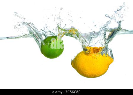 Dynamischer Spritzer einer frischen Zitrone und einer Limette, die Kräuselungen in klarem Wasser erzeugen. Stockfoto