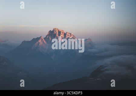 Aus der Vogelperspektive auf den majestätischen Monte Cristallo durchdringen die nebelige Luft, gemalt mit Sonnenschein, einer Symphonie aus Felsen und Himmel. Misurina, Dolomiten, Italien. Stockfoto