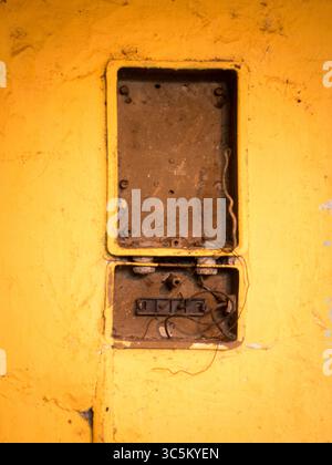 Defekter Schaltkasten an der gelben Wand. Stockfoto