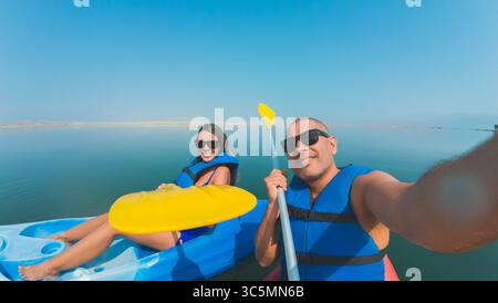 Ein Mann und eine Frau fahren mit dem Kajak auf einem See. Der Mann hält ein Paddel und die Frau trägt eine Schwimmweste. Sie lächeln und genießen die Aktivitäten Stockfoto