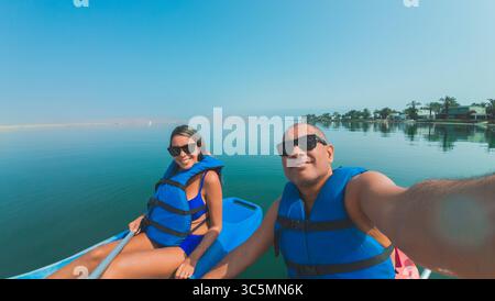 Ein Mann und eine Frau sitzen auf einem Boot im Wasser. Der Mann macht ein Foto von der Frau Stockfoto