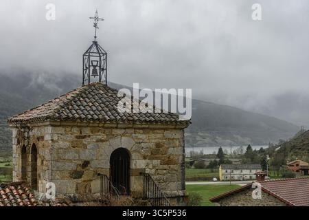 Alter Kirchturm aus Stein mit Fliesendach und Metallglocke mit Blick auf ein nebeliges Tal. Stockfoto