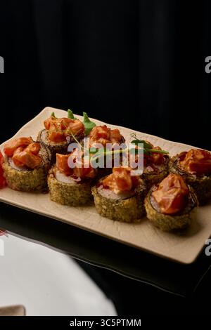 Sushi-Brötchen mit Lachs, Frischkäse und Sauce auf schwarzem Hintergrund Stockfoto