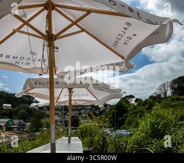 Sitzbereich im Freien mit Sonnenschirmen der Marke Salcombe Gin mit Blick auf einen malerischen Hügel und den bewölkten Himmel von Salcombe Devon Stockfoto