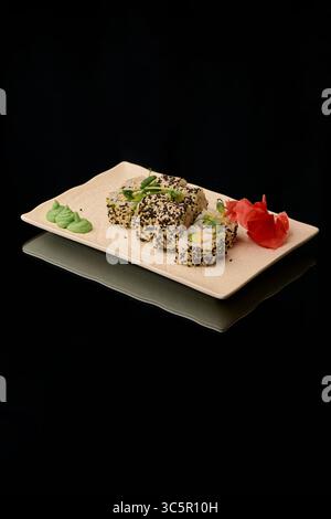 Sushi-Brötchen mit Lachs, Avocado, Gurke, Frischkäse, Nori und Sesamsamen auf schwarzem Hintergrund Stockfoto